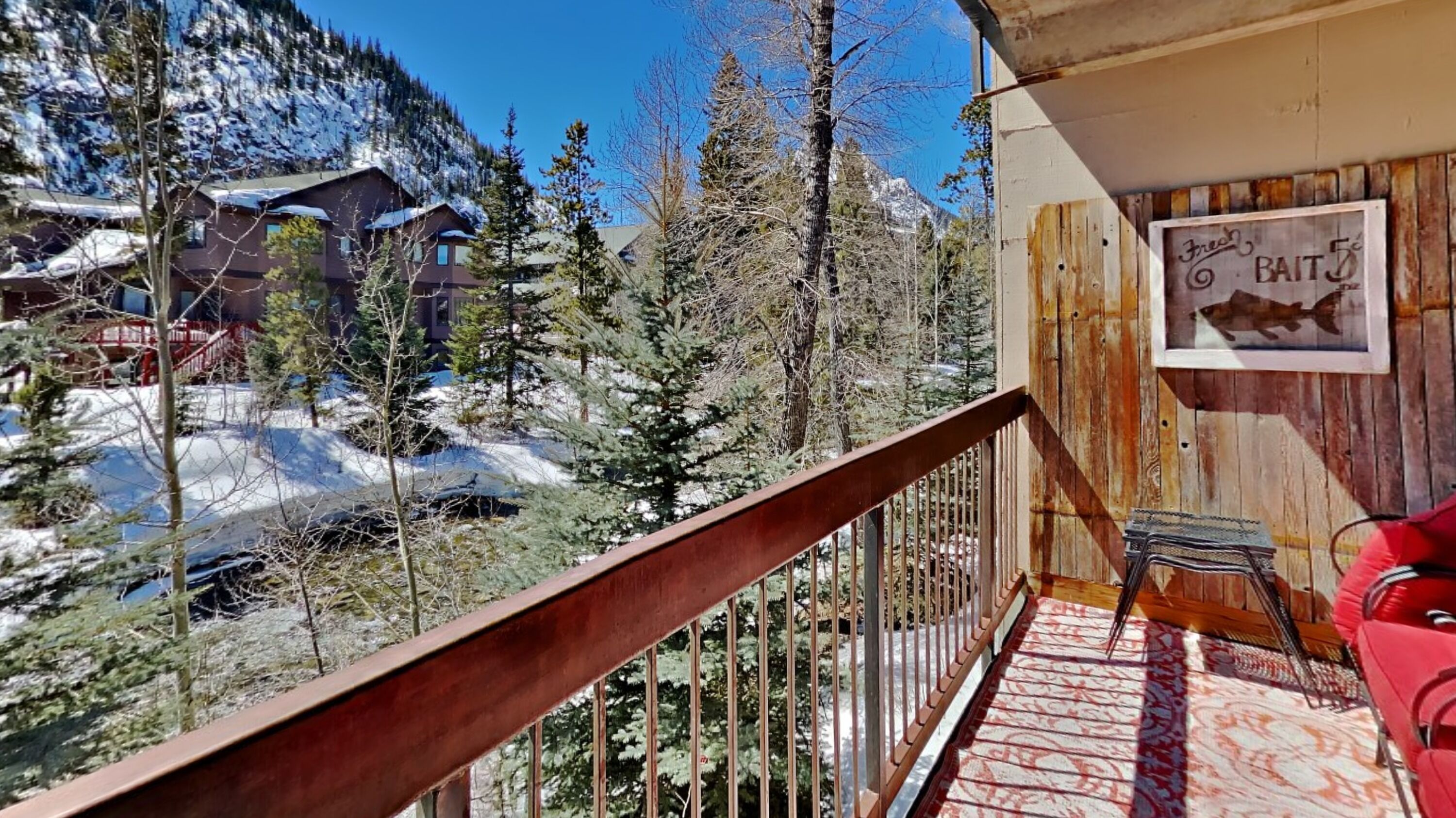 A balcony with a view of snow-covered mountains and trees, a wooden railing, and a sign that reads "Fresh Bait."