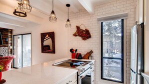 A kitchen with a large window, white brick walls, and a stainless steel refrigerator. - Creekside Condo in Downtown Frisco with Hot Tub, Pool & Mountain Views! (Frisco)
