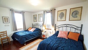 Una camera da letto con due letti, una sedia di legno, un comodino e quadri appesi al muro.