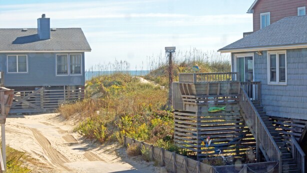 Una casa sul lungomare con un vialetto sabbioso che vi conduce, circondata da vegetazione.
