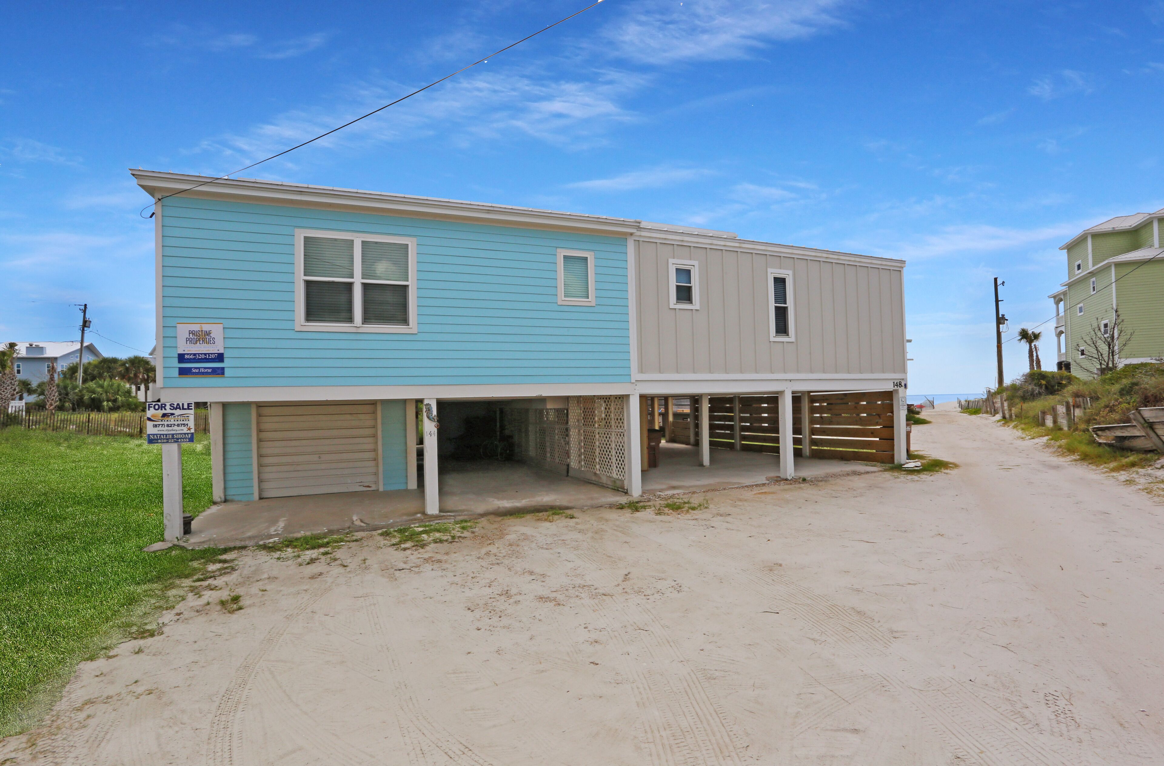 A two-story house with a garage, a covered porch, and a sandy driveway.