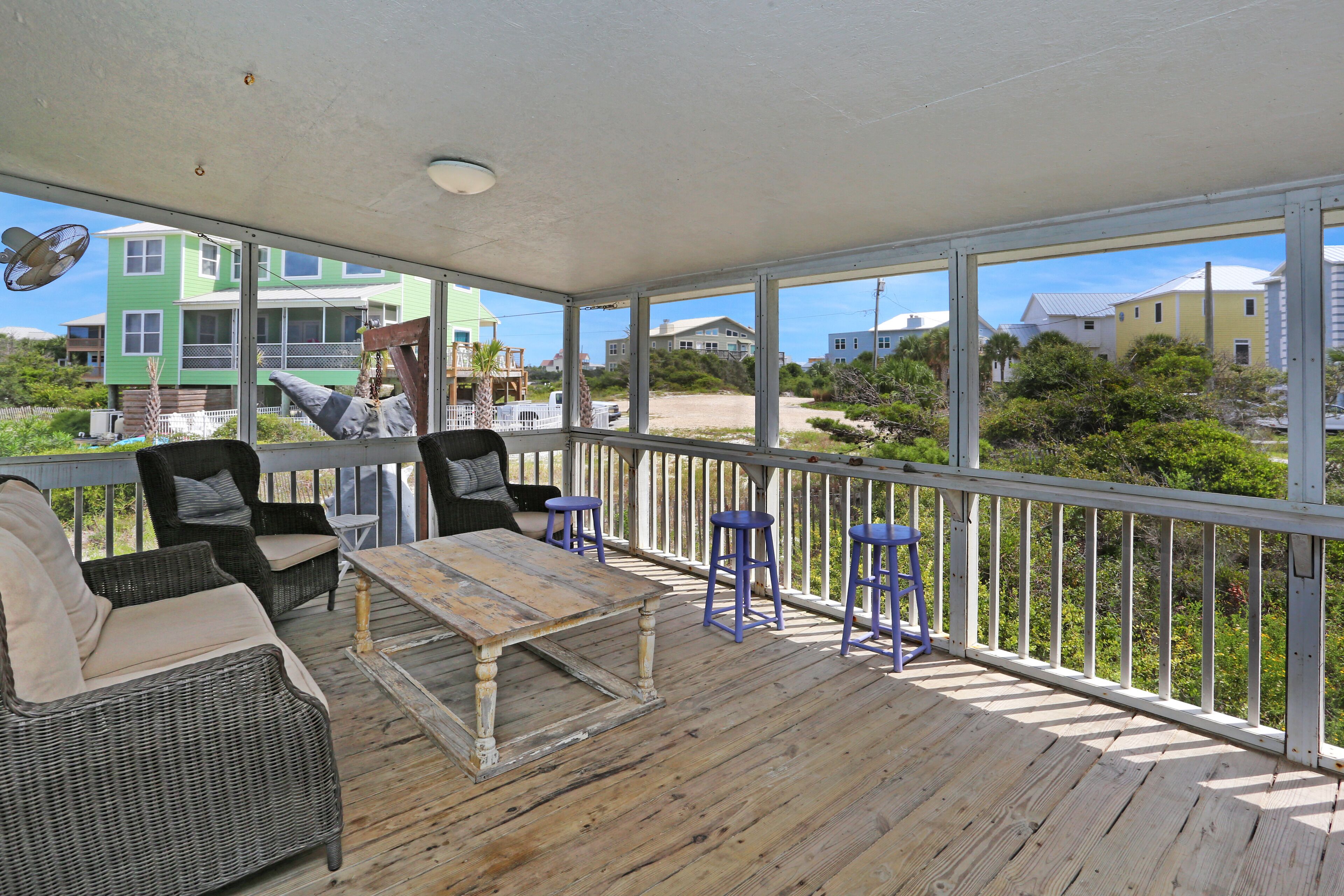 A covered outdoor deck with wicker furniture, a wooden table, and blue barstools.