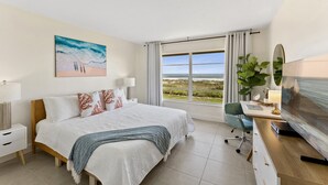 Una camera d'albergo moderna con un letto grande, una scrivania con un computer, una televisione e vista sulla spiaggia.