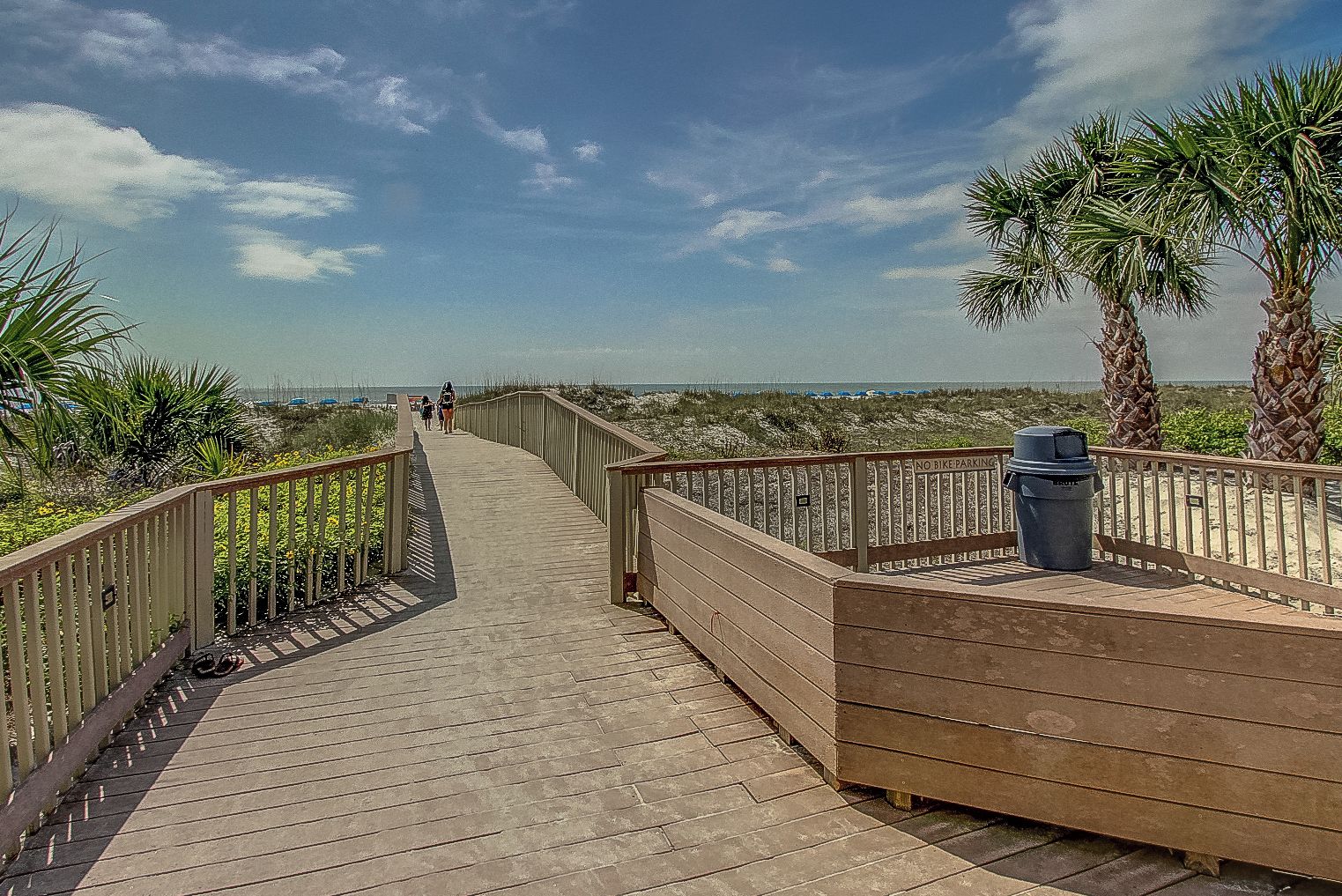 A wooden boardwalk leading to a beach with palm trees and a clear sky.