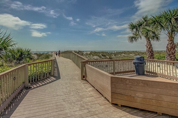 A wooden boardwalk leading to a beach with palm trees and a clear sky.