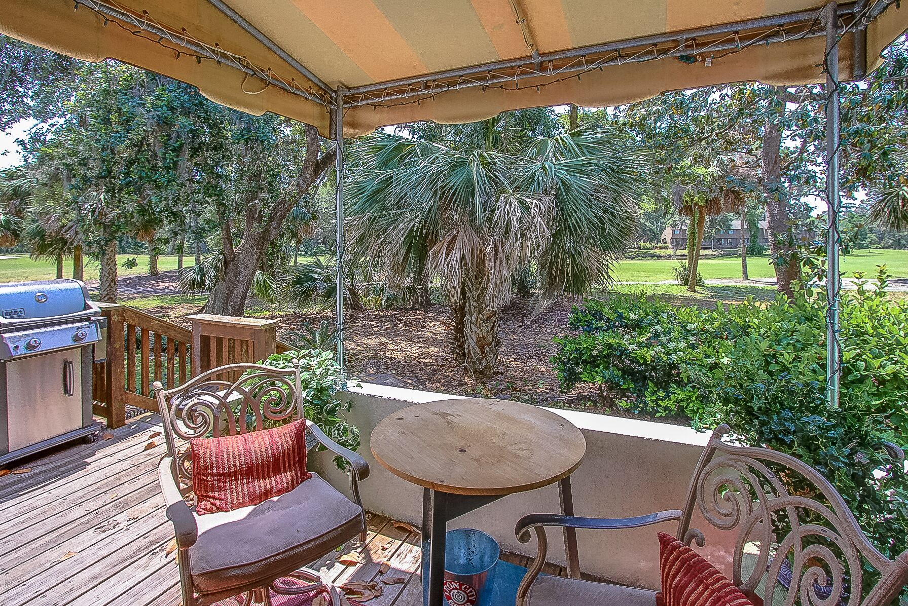An outdoor patio with a grill, wooden deck, metal chairs, and a table.