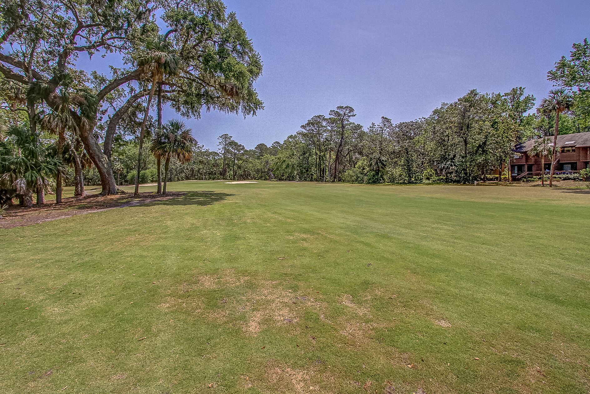 A golf course with a well-maintained green, trees, and a building in the background.