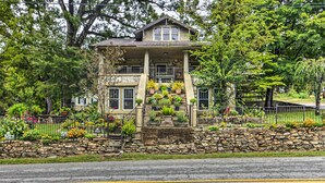 A two-story house with a stone foundation, a balcony with potted plants, and a stone wall in front. - Historic 'Hardy House' on Main Street w/ Fire Pit! (Hardy)