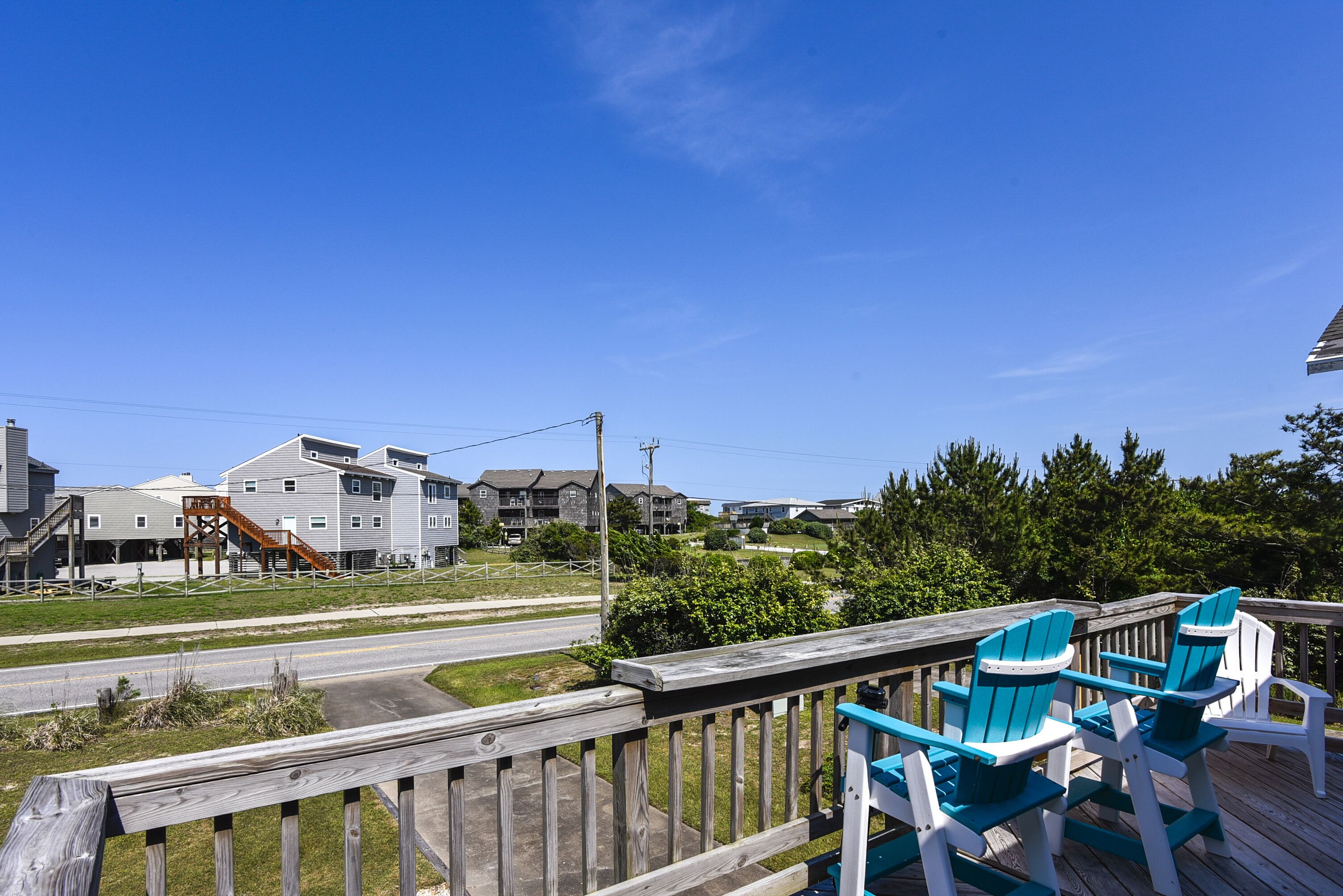 A wooden deck with blue and white Adirondack chairs, overlooking a road and residential buildings.
