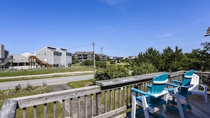 Une terrasse en bois, agrémentée de chaises Adirondack bleues et blanches, qui offre une vue sur une route et des immeubles d’habitation.