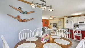 Un coin repas avec une table en bois, des chaises blanches et un ventilateur de plafond.