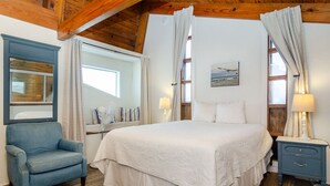 Un dormitorio con una cama grande, un sillón azul, una mesita de noche y una ventana con cortinas.
