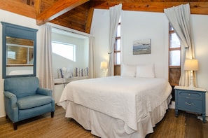 Ein Schlafzimmer mit einem großen Bett, einem blauen Sessel, einem Nachttisch und einem Fenster mit Vorhängen.