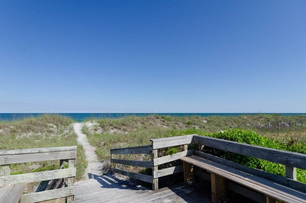 A wooden boardwalk leading to a beach with a clear sky.