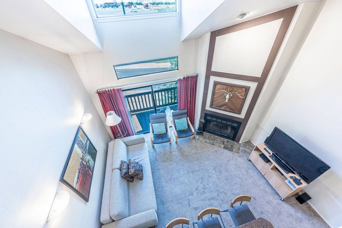 A high-ceilinged living area with a sofa, chairs, a fireplace, and a television.