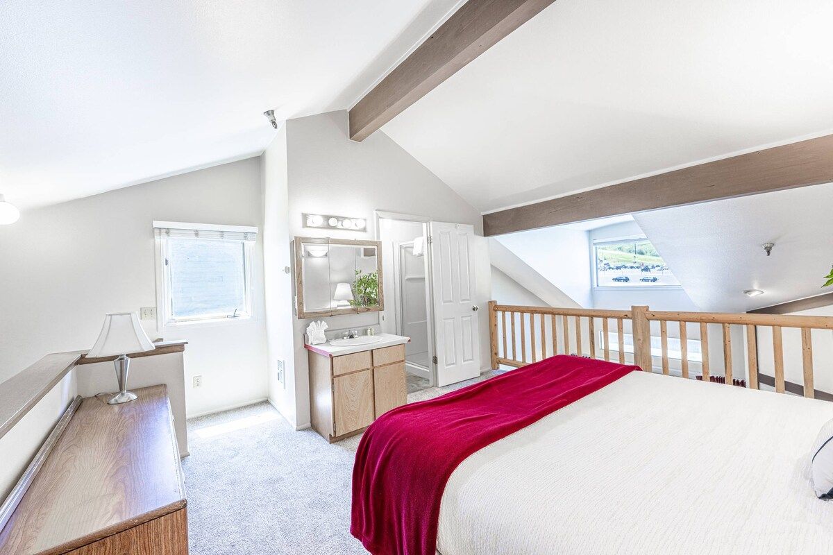 A bedroom with a bed, a vanity with a mirror, a window, and a balcony.