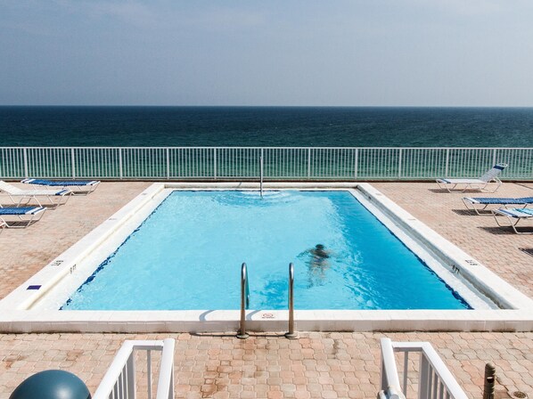 A rectangular pool with clear blue water, surrounded by a white pool deck. There are lounge chairs and a lifeguard stand.