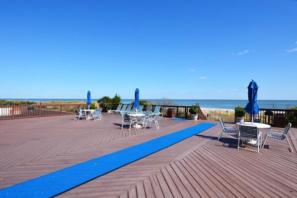 Une terrasse en bois avec des chaises et des parasols bleus, donnant sur la plage.