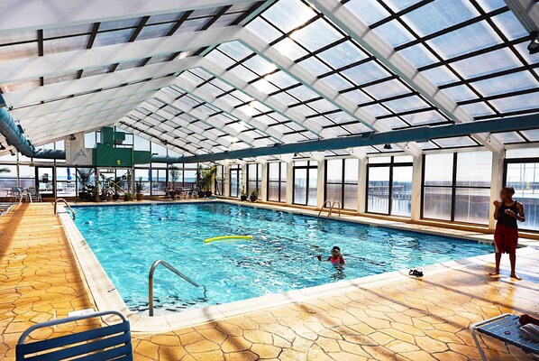 An indoor swimming pool with clear glass ceilings, a tiled floor, and a view of the outside.