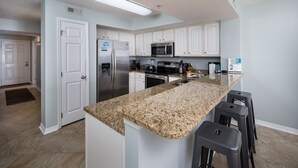A modern kitchen with white cabinets, granite countertops, stainless steel appliances, and a central island with bar stools.