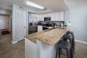 A modern kitchen with white cabinets, granite countertops, stainless steel appliances, and a central island with bar stools.
