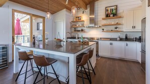 A modern kitchen with a large island, bar stools, wooden ceiling, and white cabinetry.