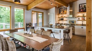 A modern kitchen with wooden beams, large windows, and a dining area with wicker chairs.