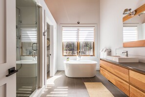 A modern bathroom with a glass shower enclosure, a freestanding bathtub, and a vanity with a mirror.