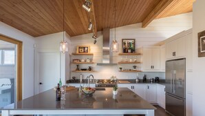 A modern kitchen with a large island, wooden ceiling, and white cabinetry.