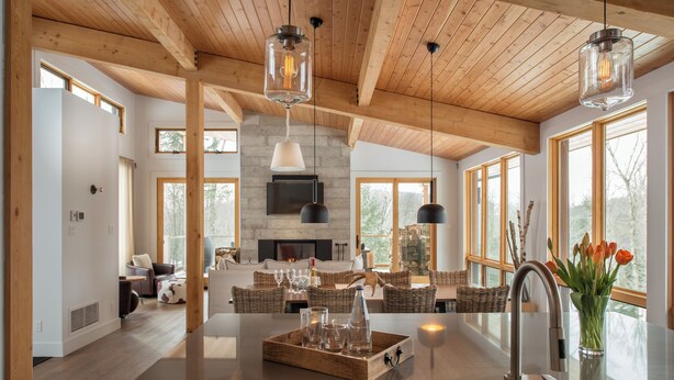 A spacious kitchen with a central island, wooden ceiling beams, large windows, and a fireplace.