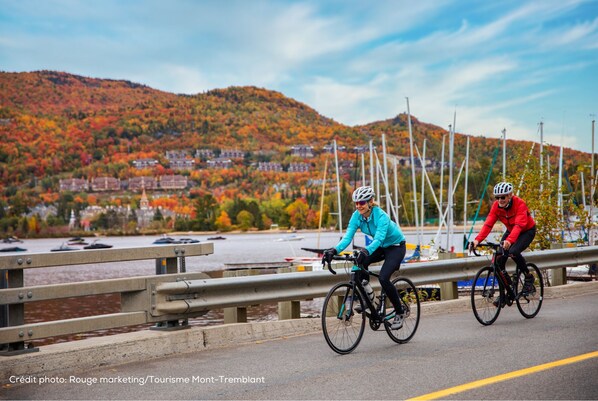 Two cyclists on a bridge with a scenic view of a town and mountains in the background.