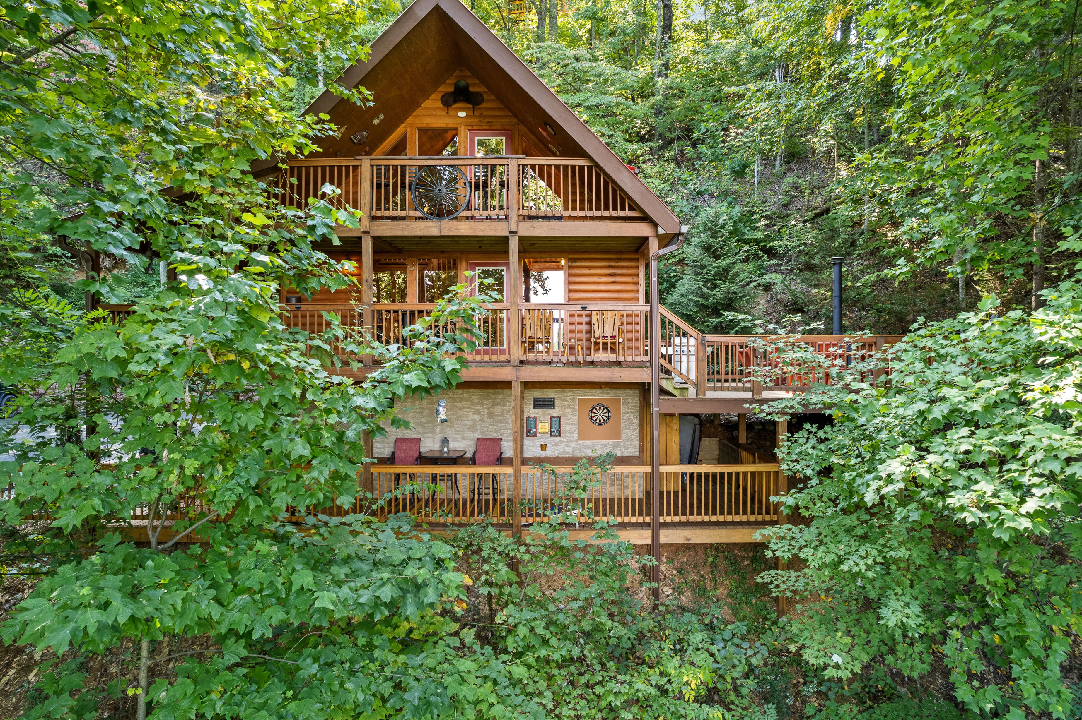 A multi-story log cabin with a balcony, surrounded by dense forest.
