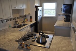 A modern kitchen with white cabinets, a stainless steel refrigerator, a built-in oven, and a window providing natural light.