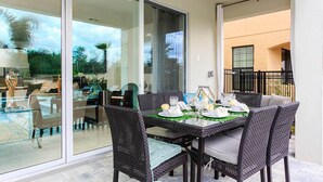 Un espace extérieur aménagé pour les repas, avec des chaises en osier et une table en verre, le tout disposé pour accueillir quatre personnes.