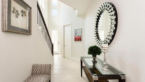 Un couloir avec un escalier, un banc, une console surmontée d’un miroir et un tableau encadré accroché au mur.