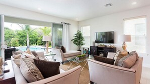 Un salon moderne avec vue sur la piscine, doté de sièges confortables et d’un téléviseur à écran plat.