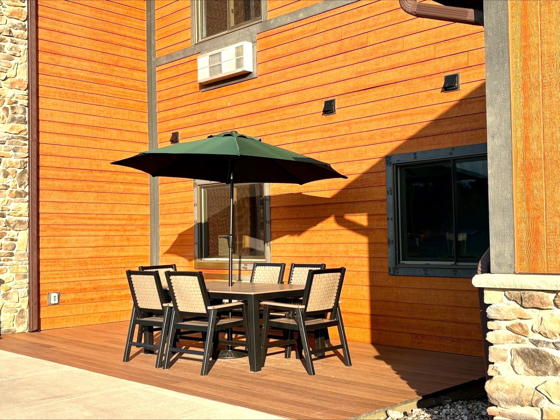 Un patio esterno con tavolo e sedie, un ombrello verde e un muro in pietra.