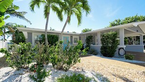 A modern house with a covered patio, a blue door, and a well-maintained garden with various plants and a gravel driveway. - Private Pool, Pets & Beach Days Just Steps Away (Holmes Beach)