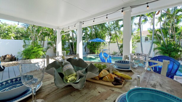 An outdoor dining area with a pool view, featuring a table with food, drinks, and a bottle of champagne. - Private Pool, Pets & Beach Days Just Steps Away (Holmes Beach)