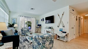 A living room with a blue and white patterned sofa, a coffee table, and a TV mounted on the wall. There is a fireplace with a mantel, a door with a doorknob, and a ceiling vent. - Private Pool, Pets & Beach Days Just Steps Away (Holmes Beach)