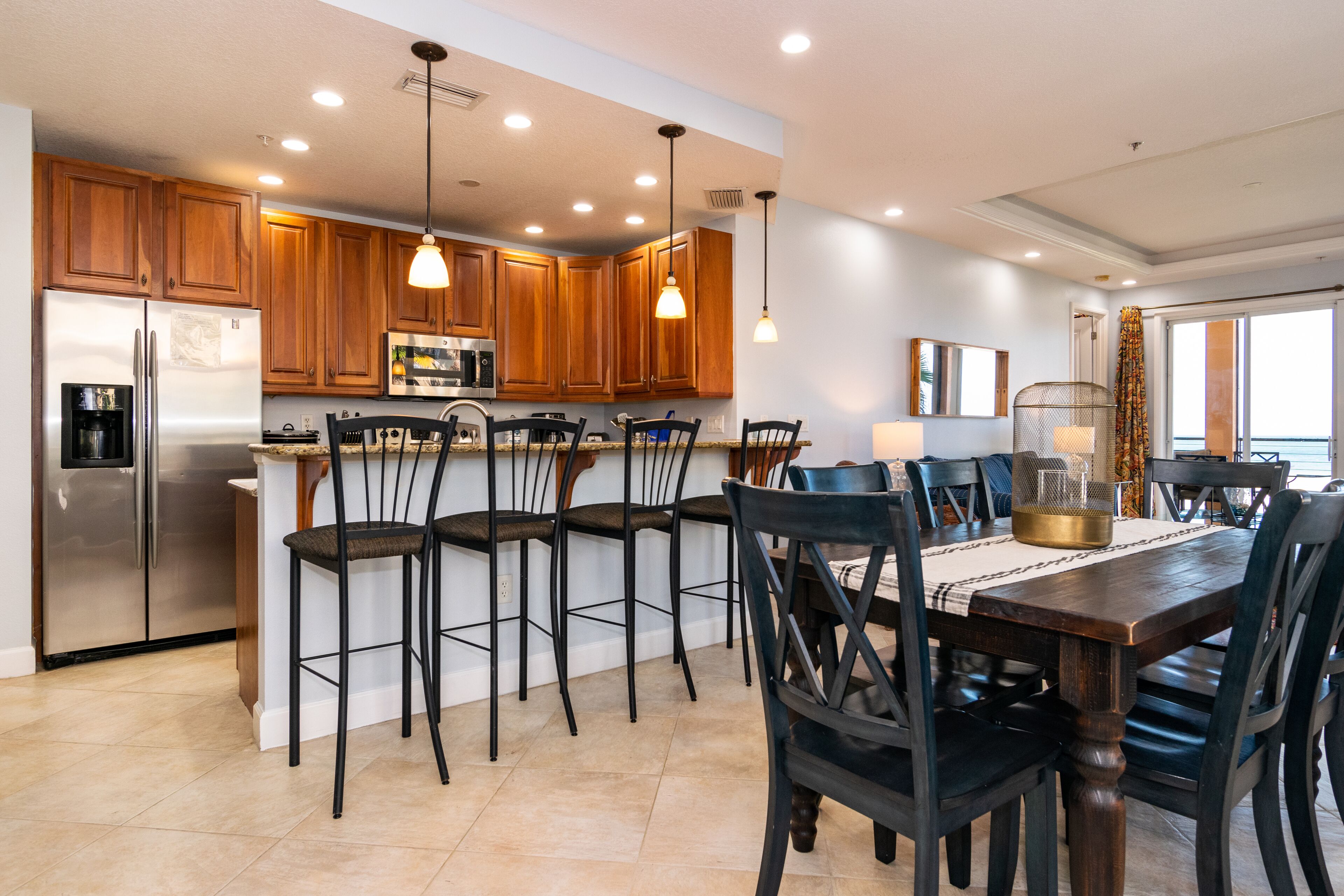 A modern kitchen with wooden cabinets, a stainless steel refrigerator, and a dining area with a table and chairs.