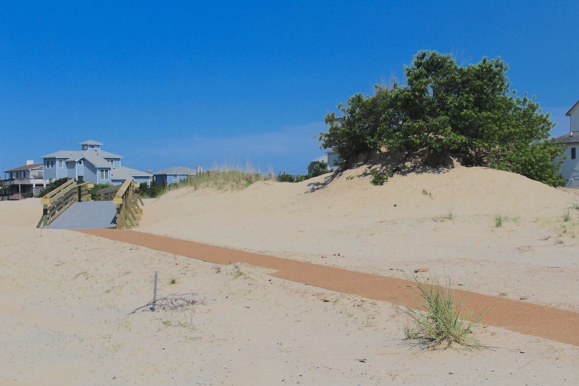 Una playa arenosa con un camino de madera que lleva a una casa de techo azul.