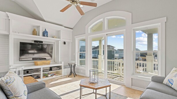 A spacious living room with a large TV, comfortable seating, and a balcony with a view. - Coastal Calling at Corolla Shores 7 Bedroom Home, Near Beach Access + Private Pool (Corolla)
