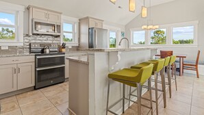 A modern kitchen with a central island, stainless steel appliances, and a bar area with stools. - Coastal Calling at Corolla Shores 7 Bedroom Home, Near Beach Access + Private Pool (Corolla)