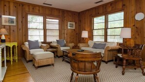 A cozy room with wooden walls, wicker furniture, and large windows with blinds.