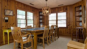 A wooden-paneled room with a large dining table, chairs, and a hanging light fixture.