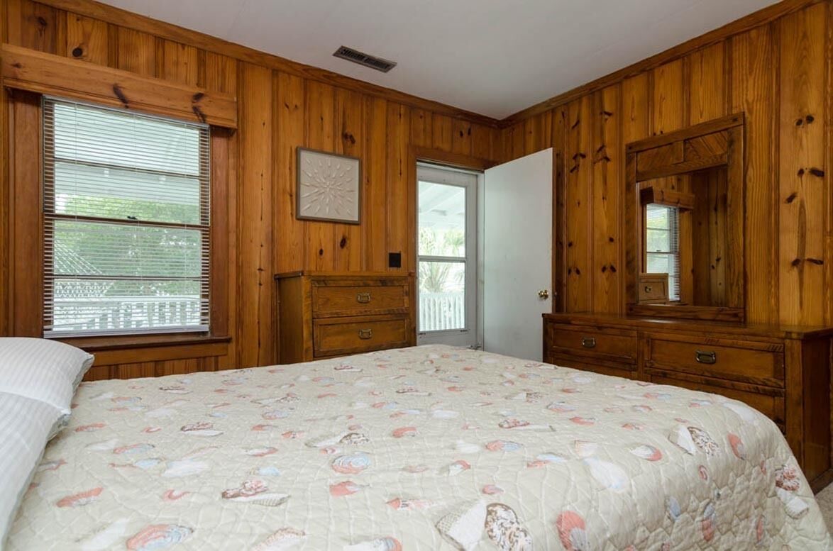 A bedroom with wooden paneling, a bed with a floral quilt, a dresser, and a large mirror.