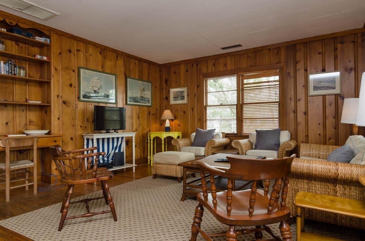 A wooden-paneled room with a television, a dining table, and a sofa.