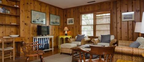 A wooden-paneled room with a television, a dining table, and a sofa.