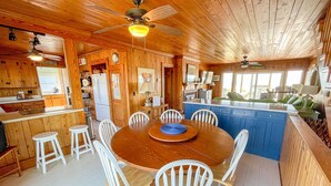 A wooden cabin interior with a dining area, kitchen, and a large window. - Barnacle: Pet-Friendly Ocean Escape (Topsail Beach)